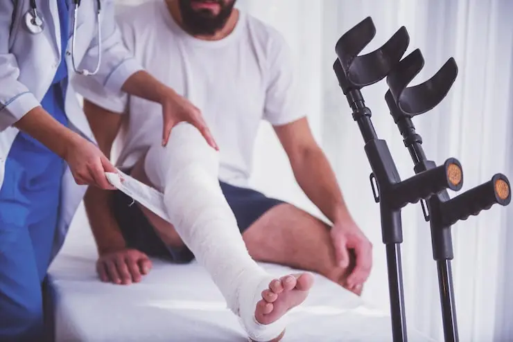 Clinician attending to a patient's injured leg with crutches beside the treatment table