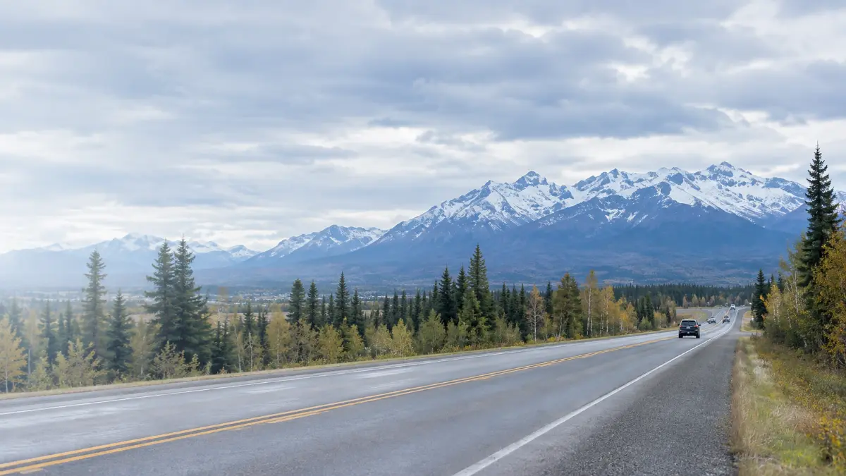 Highway through the Mat-Su Valley with autumn trees and snow-covered mountains